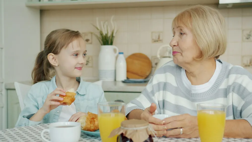 A grandmother and her granddaughter talking over breakfast at the kitchen table.